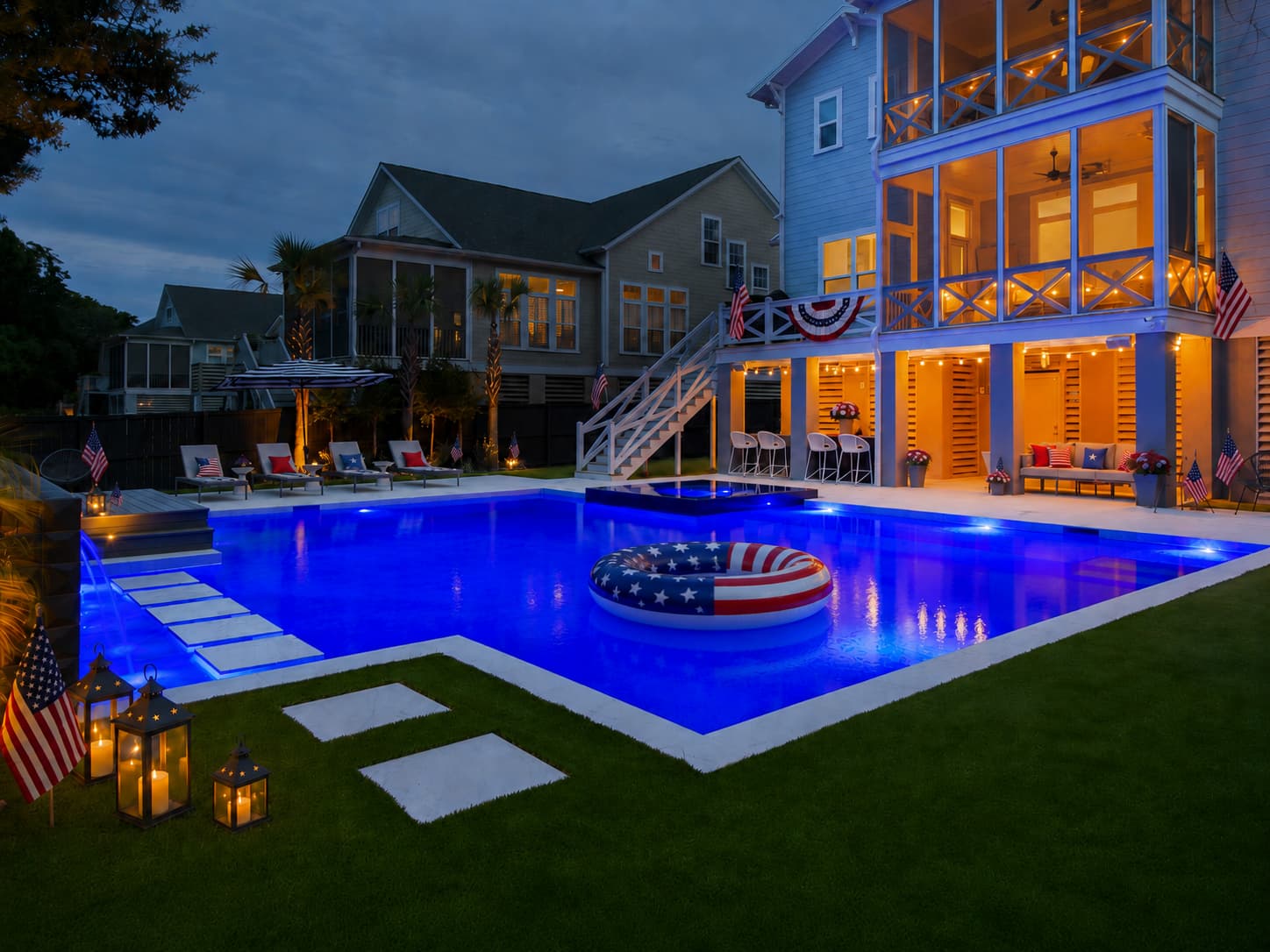 Backyard pool at dusk decorated for the 4th of July with an American flag float, patriotic bunting, and lit lanterns.