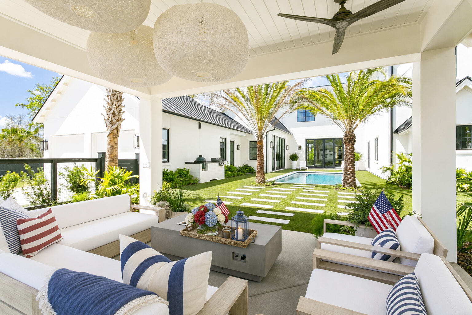 Modern covered patio decorated for a 4th of July pool party with American flag pillows and red, white, and blue florals.