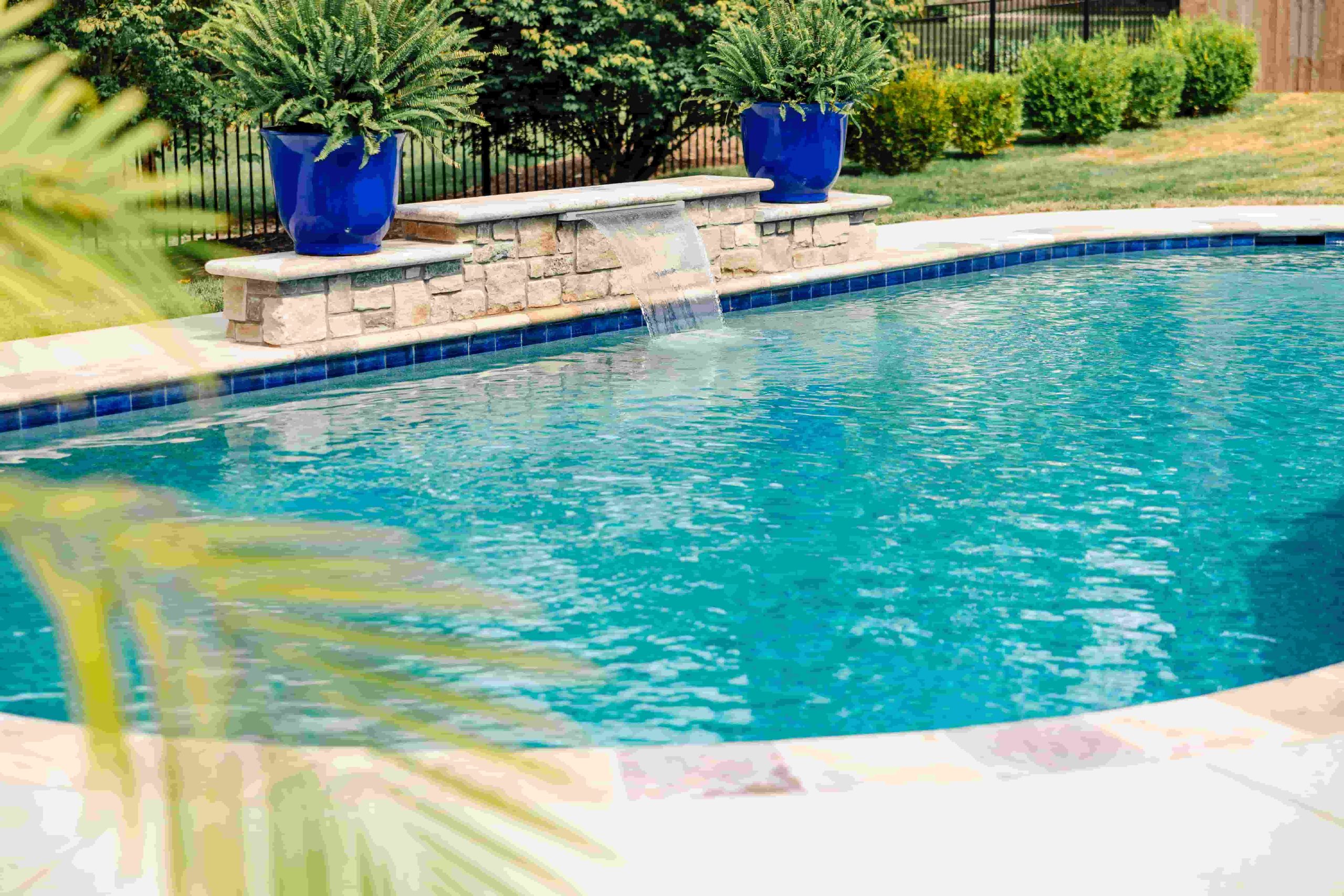 Backyard swimming pool with a sheer descent waterfall feature flanked by cobalt blue ceramic planters