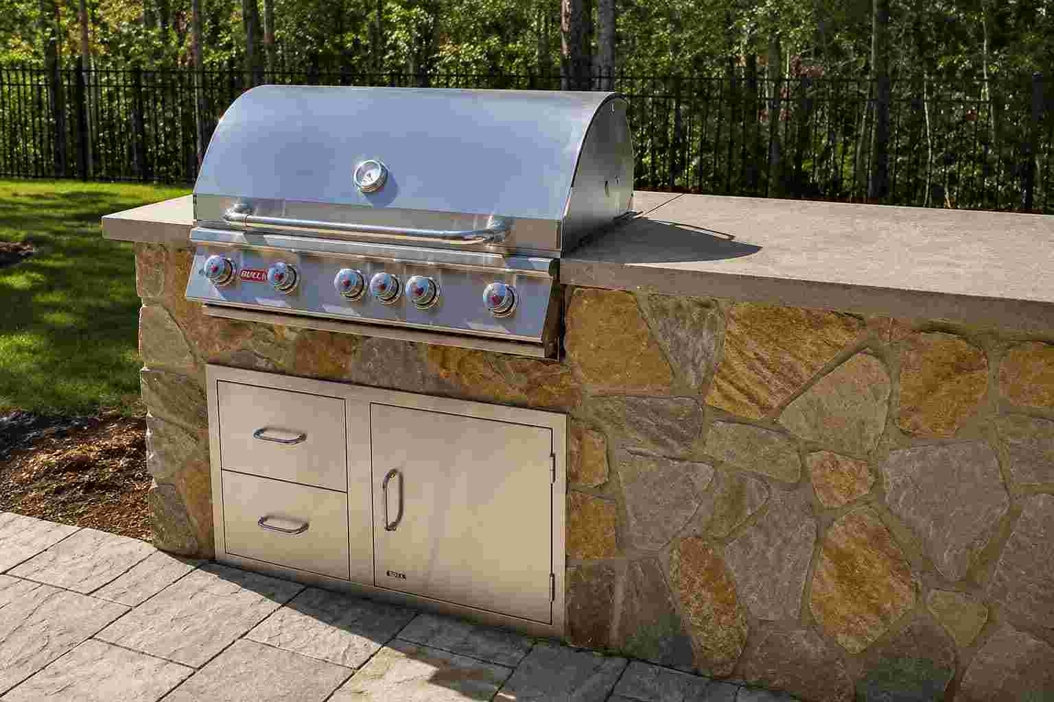Stainless steel built-in gas grill set into a flagstone outdoor kitchen island with concrete countertop.