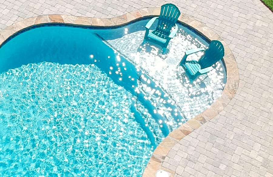 Aerial view of a pool tanning ledge with two teal Adirondack chairs in shallow water