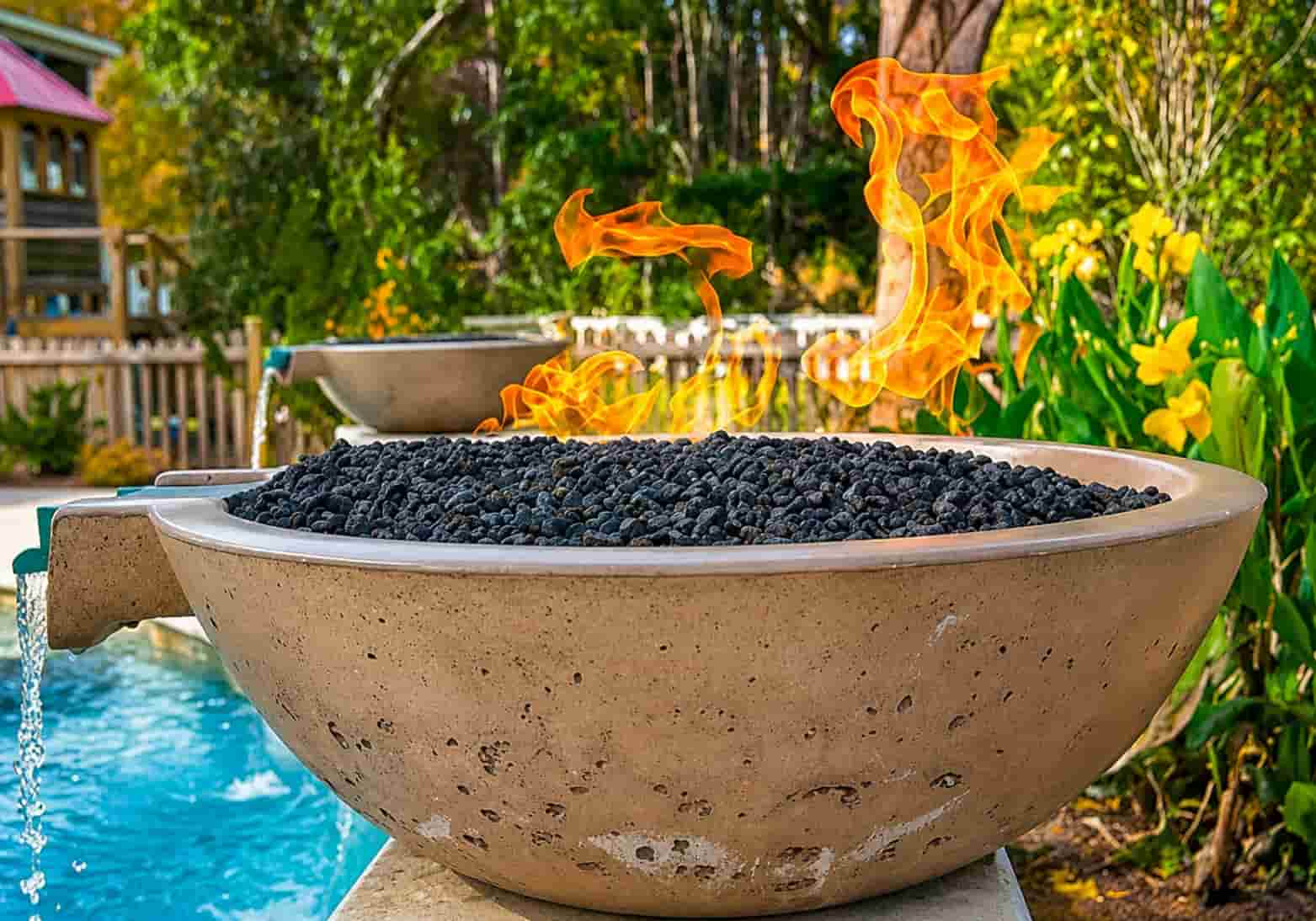 close-up of a concrete combination fire and water bowl with lava rocks spilling water into a pool in a tropical backyard