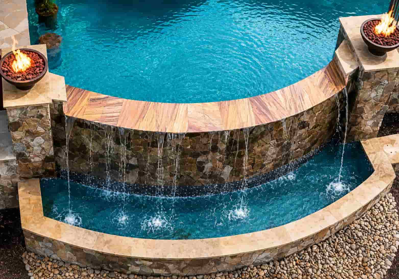 aerial view of a curved stone pool waterfall wall flanked by two fire bowls with lava rocks