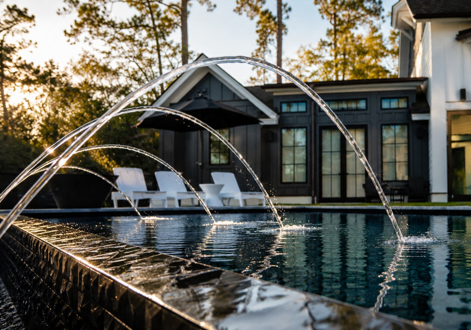 Multiple deck jets shooting arcing streams over a dark-tiled contemporary pool at golden hour