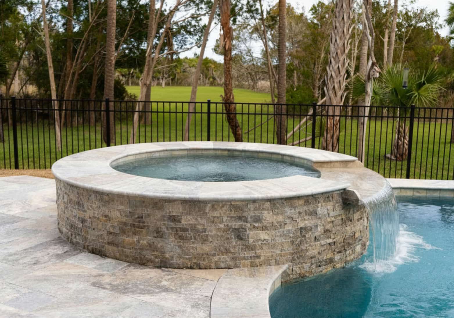 Elevated round spa with stone veneer and spillover waterfall flowing into a Blue Haven inground pool
