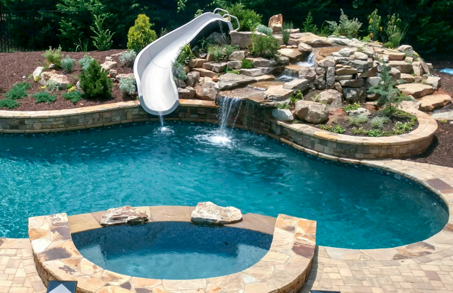Freeform pool and spa with stone waterfall and white slide built into landscaped rock feature