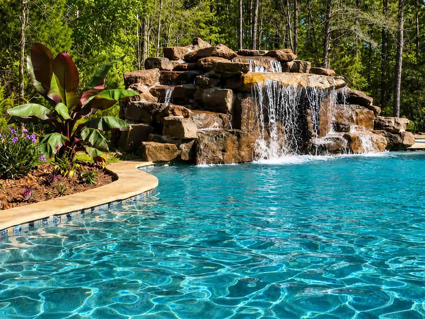 Grotto-style rock waterfall cascading into a backyard inground swimming pool
