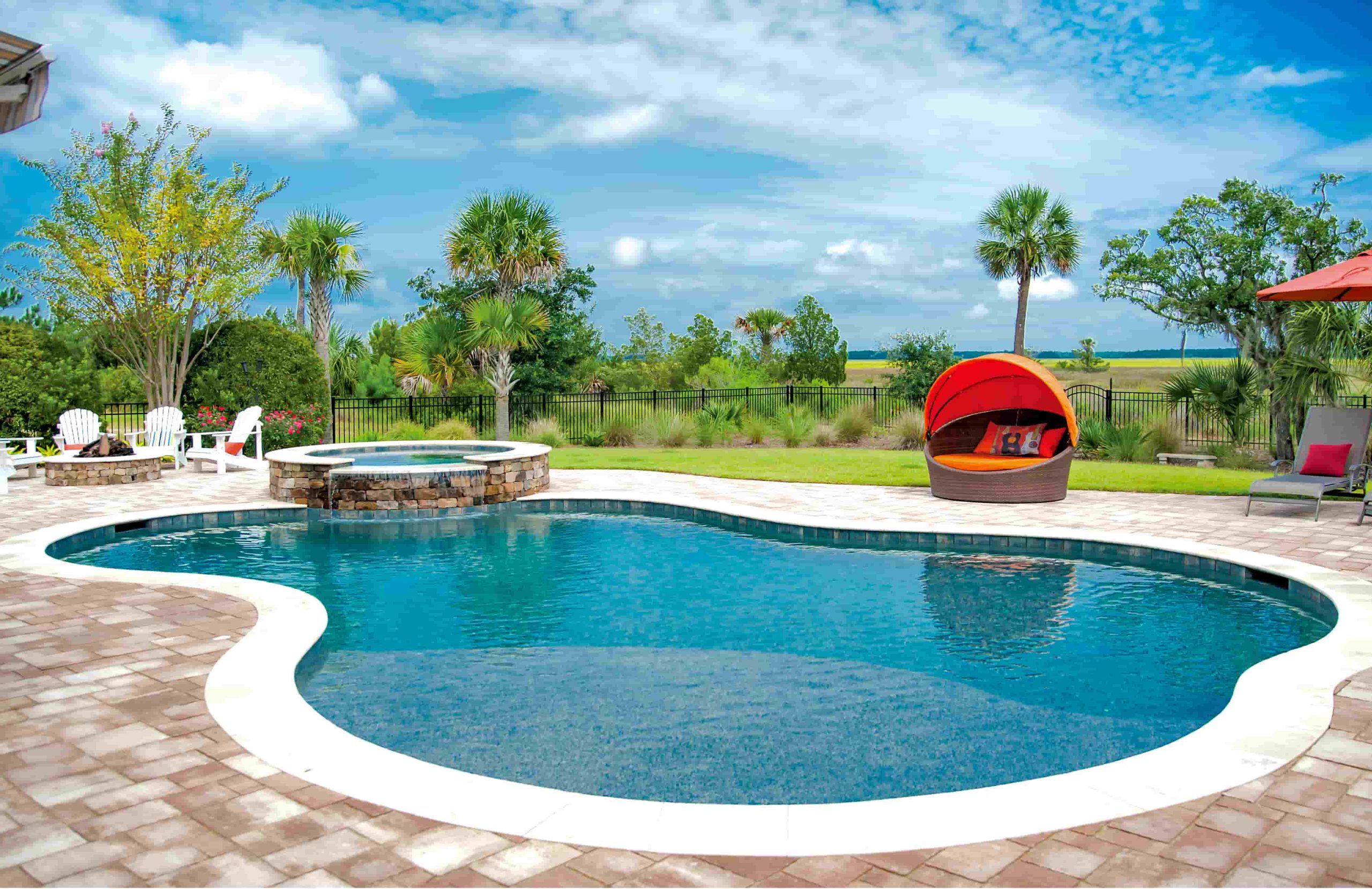 Freeform gunite pool with attached spa, paver decking, and tropical landscaping in a residential backyard