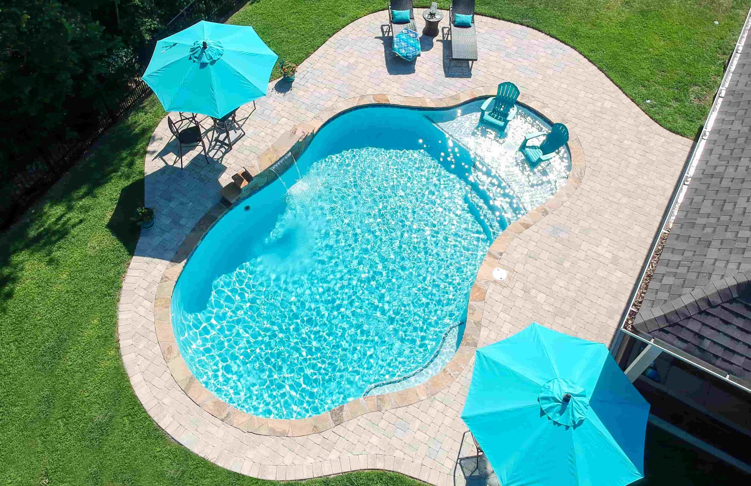 Aerial view of a gunite pool with tanning ledge, paver patio, and outdoor seating area