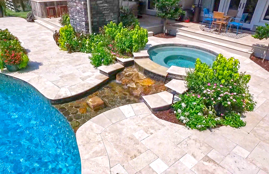 Raised spa spillover flowing into a tropical freeform swimming pool