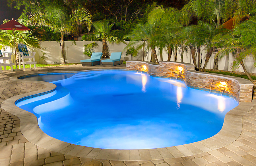 Blue LED pool lighting illuminating a custom pool with three cascade waterfalls and ledger stone bond beam at night