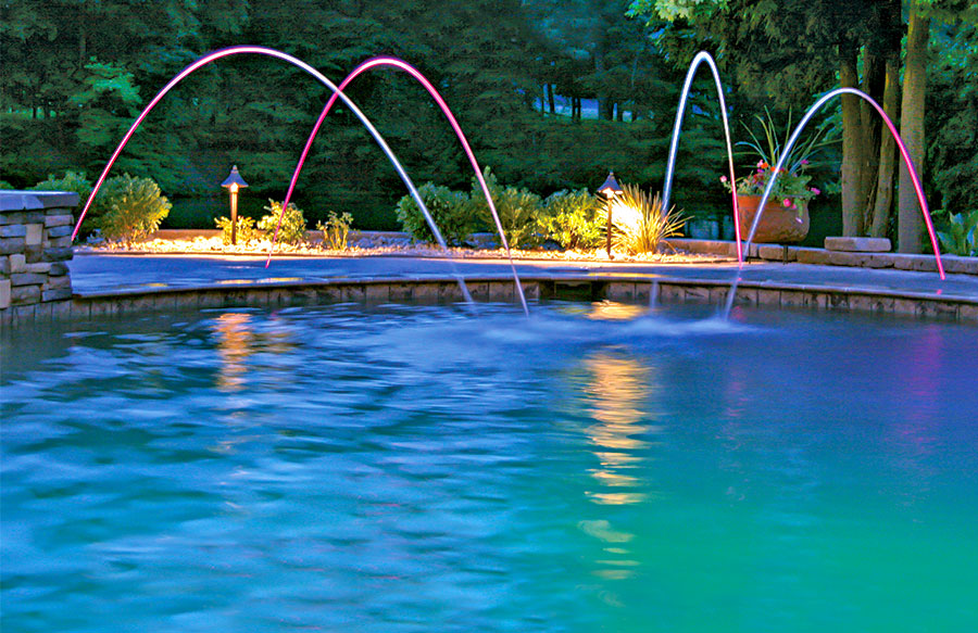 LED-lit laminar water jets arcing into a custom pool at night