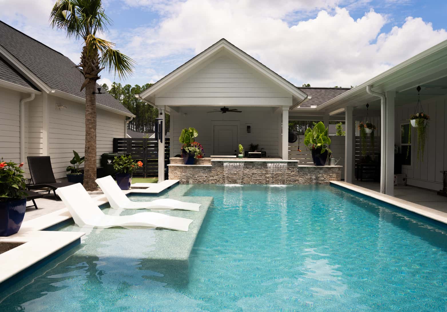 White in-pool lounge chairs on a tanning ledge in a Blue Haven rectangular inground pool with outdoor kitchen