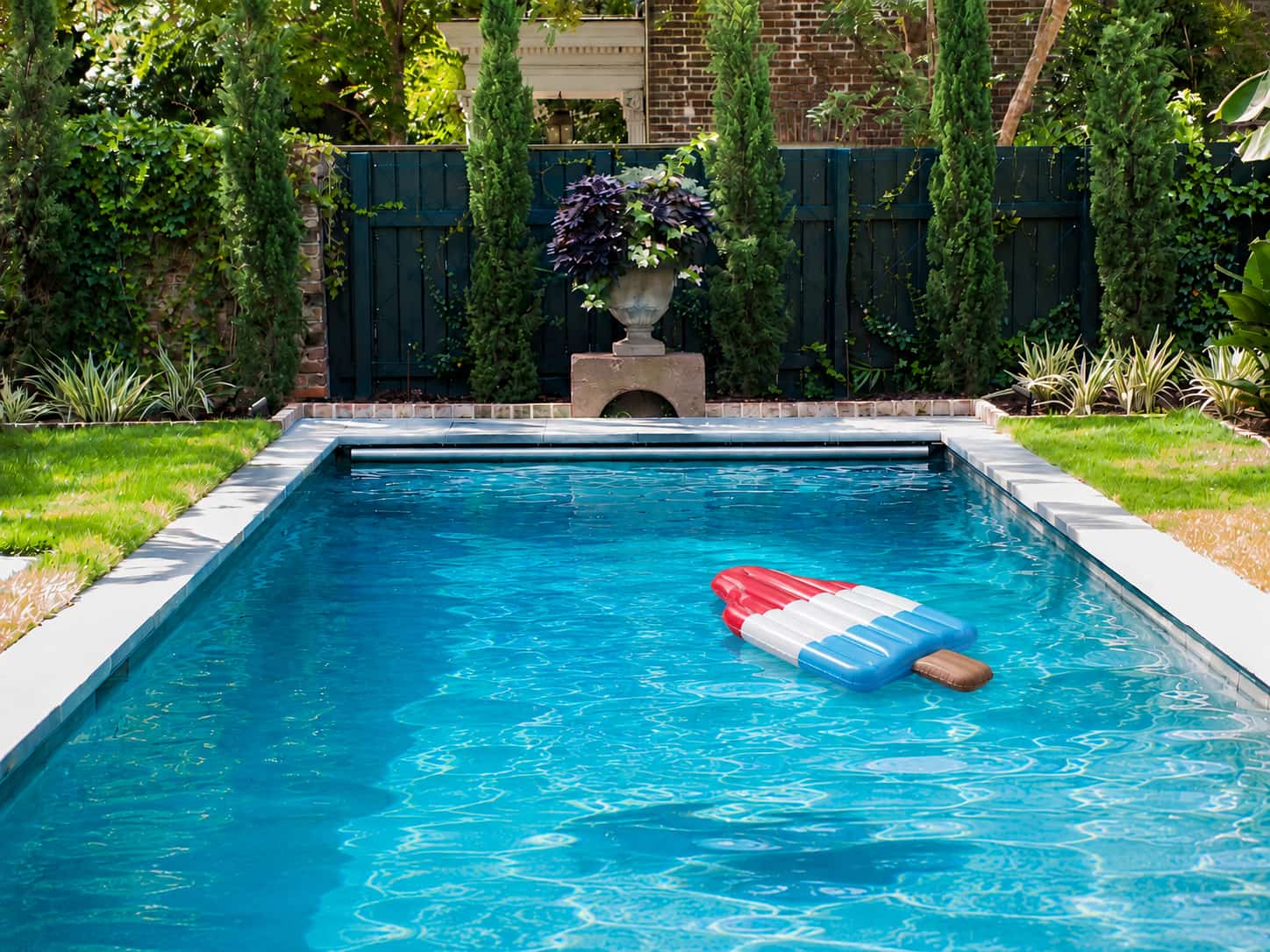 nflatable red, white, and blue ice pop pool float drifting in a landscaped backyard swimming pool