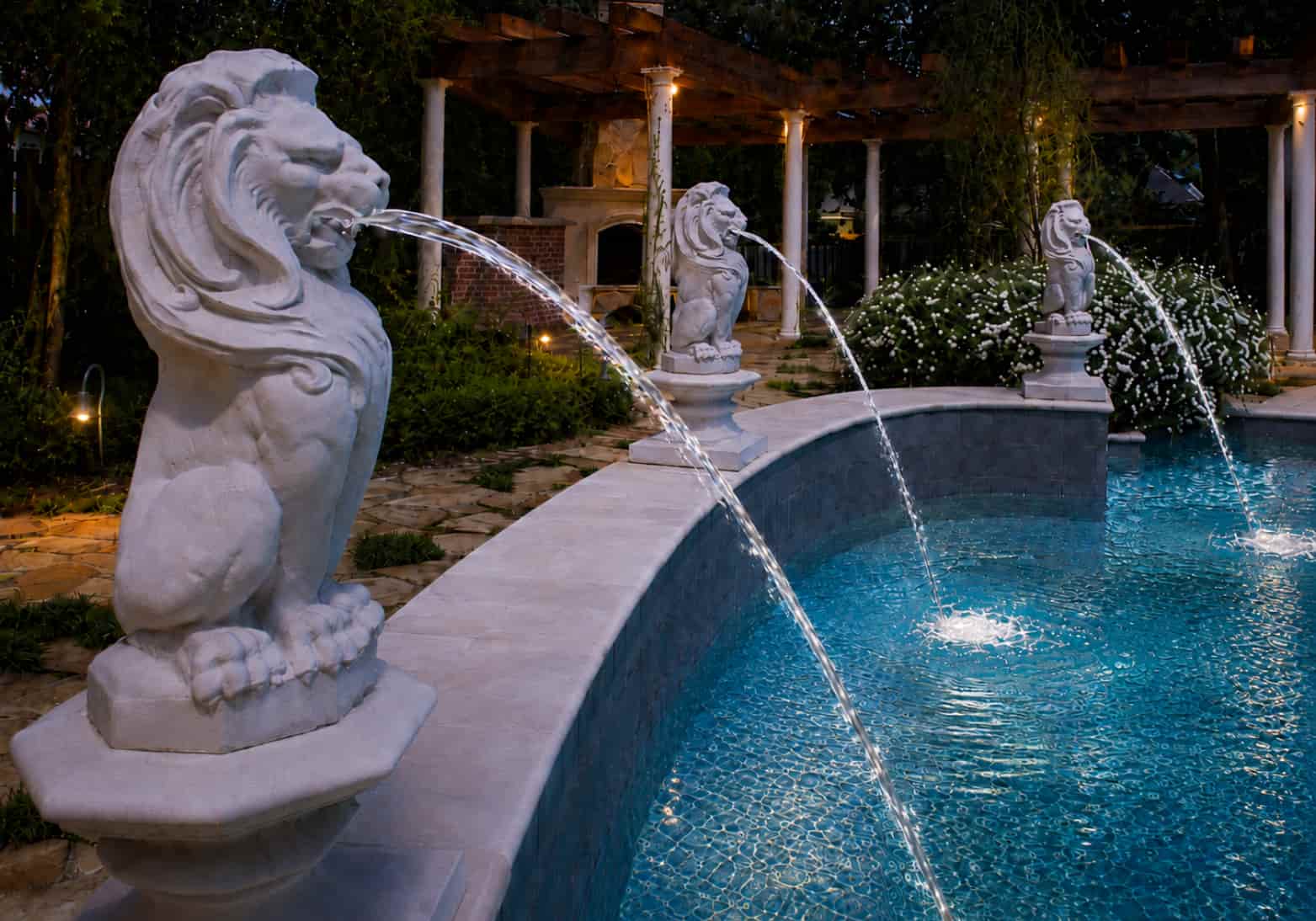Three lion spouting statues shooting arcing water streams into an elegant curved pool at night