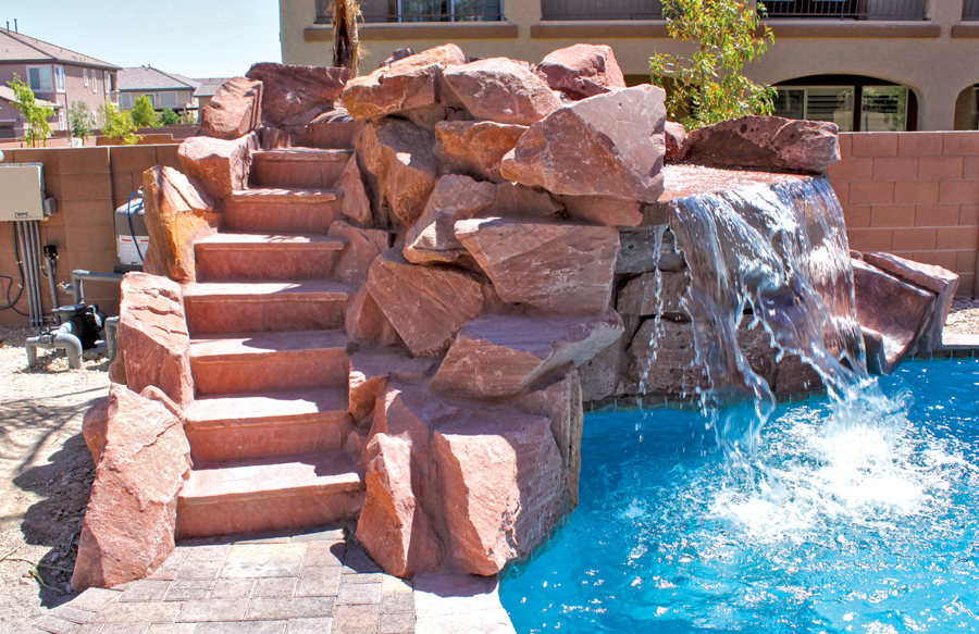 Stone staircase leading to rock waterfall feature spilling into a backyard swimming pool