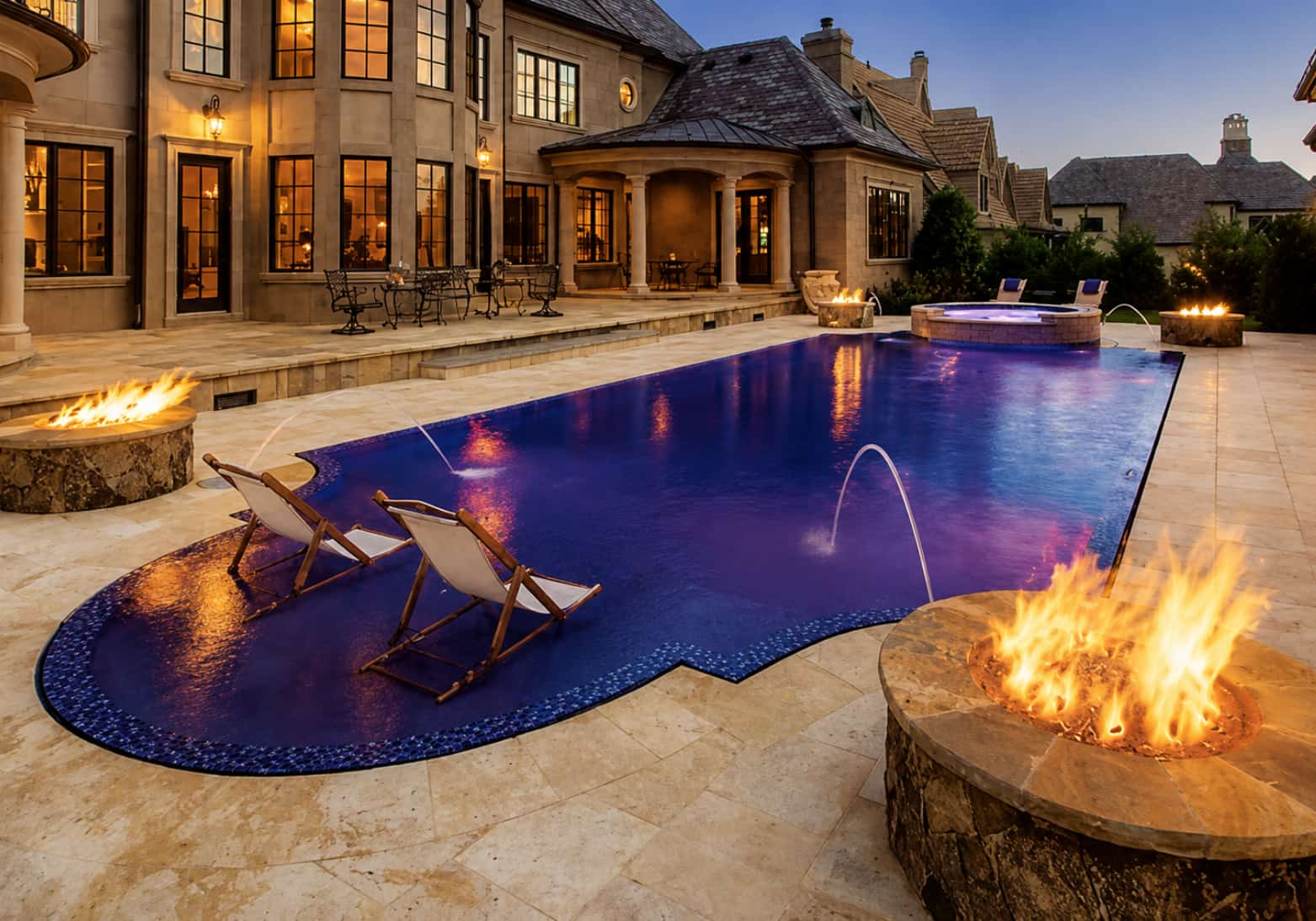 Multiple fire pits flanking luxury pool at dusk on travertine deck