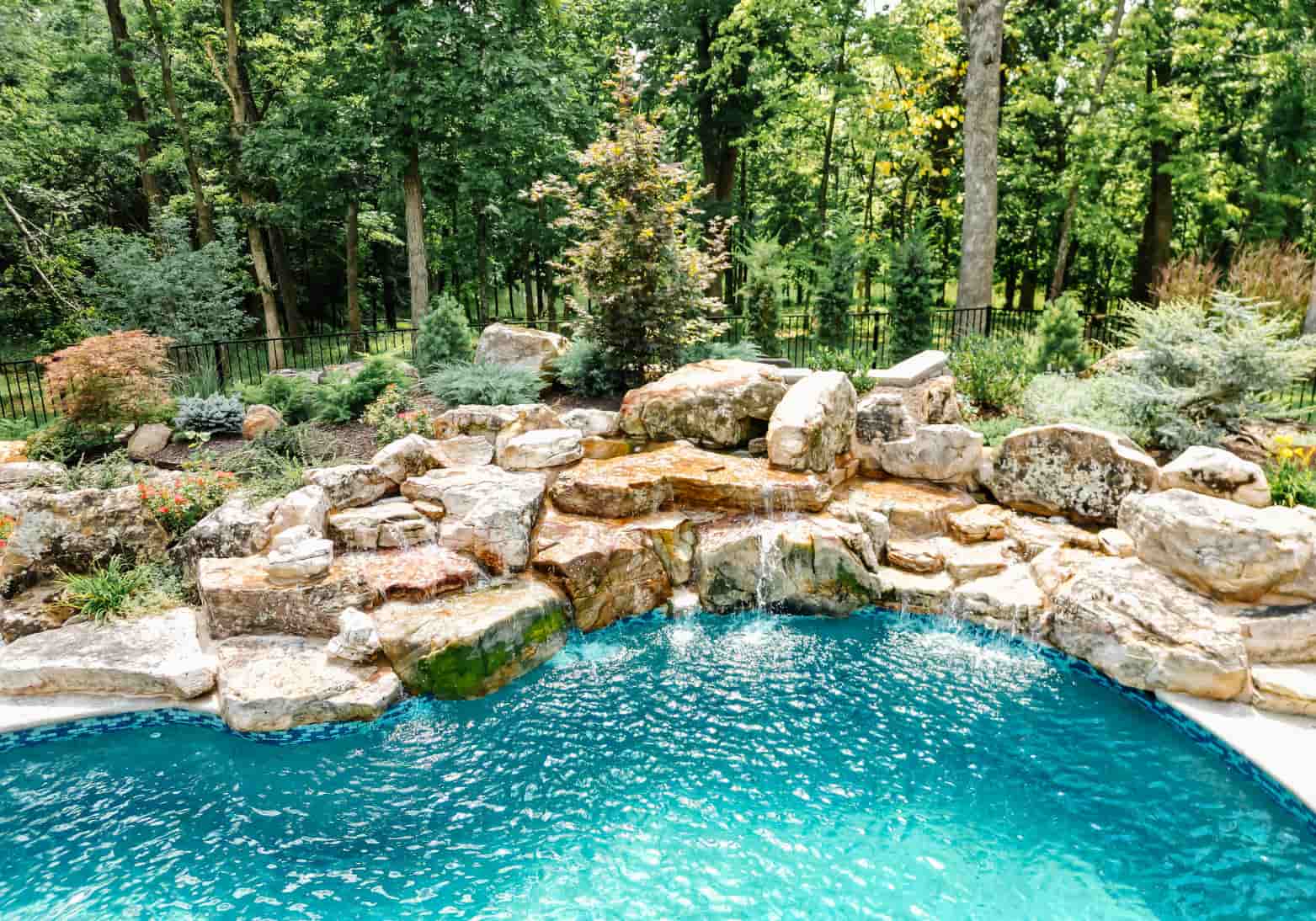 Large natural rock waterfall cascading into a Blue Haven inground pool surrounded by mature landscaping