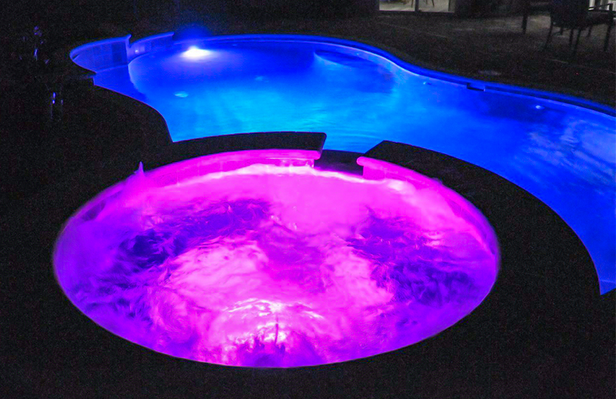 Custom pool with hot pink spa lighting and cool blue pool lighting at night