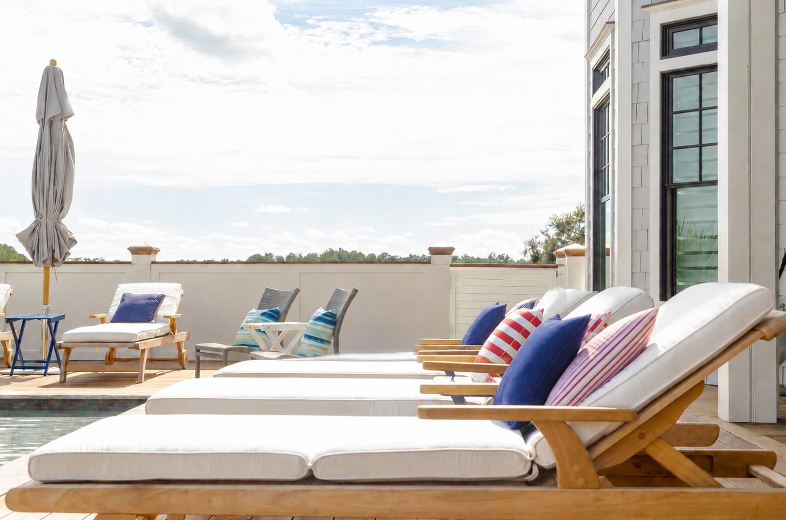 Poolside teak loungers styled with red, white, and blue pillows for a 4th of July pool party.