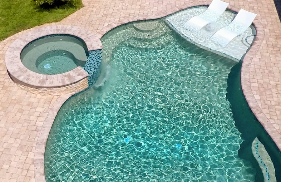 Aerial view of pool sun shelf with white chaise lounge positioned next to an attached spa
