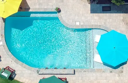 small backyard pool with tanning ledge and in-water lounge chairs under umbrellas