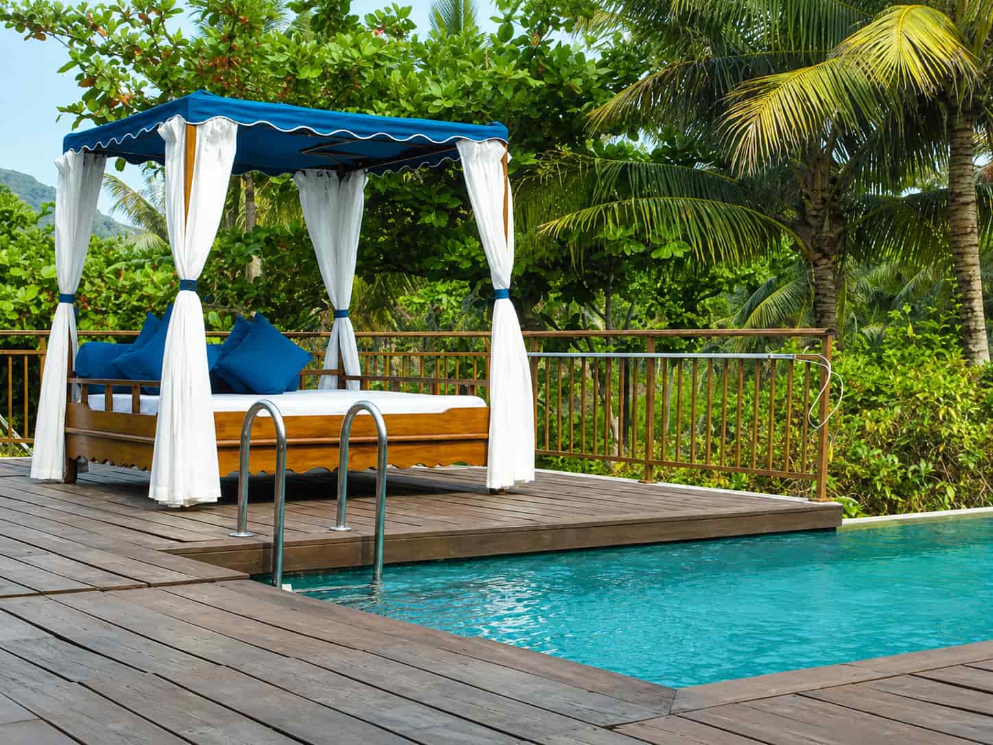 Poolside cabana with blue canopy and white curtains next to an inground pool