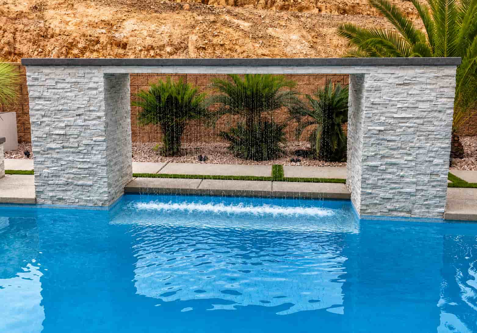 Rain curtain water feature on a white stacked stone frame dropping into a bright blue pool