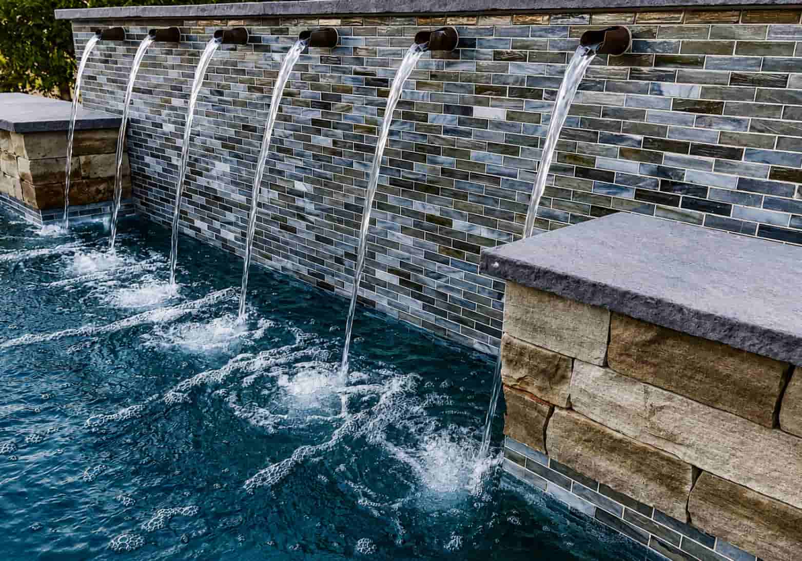 Six round bronze scuppers mounted on a decorative glass tile pool bond beam wall