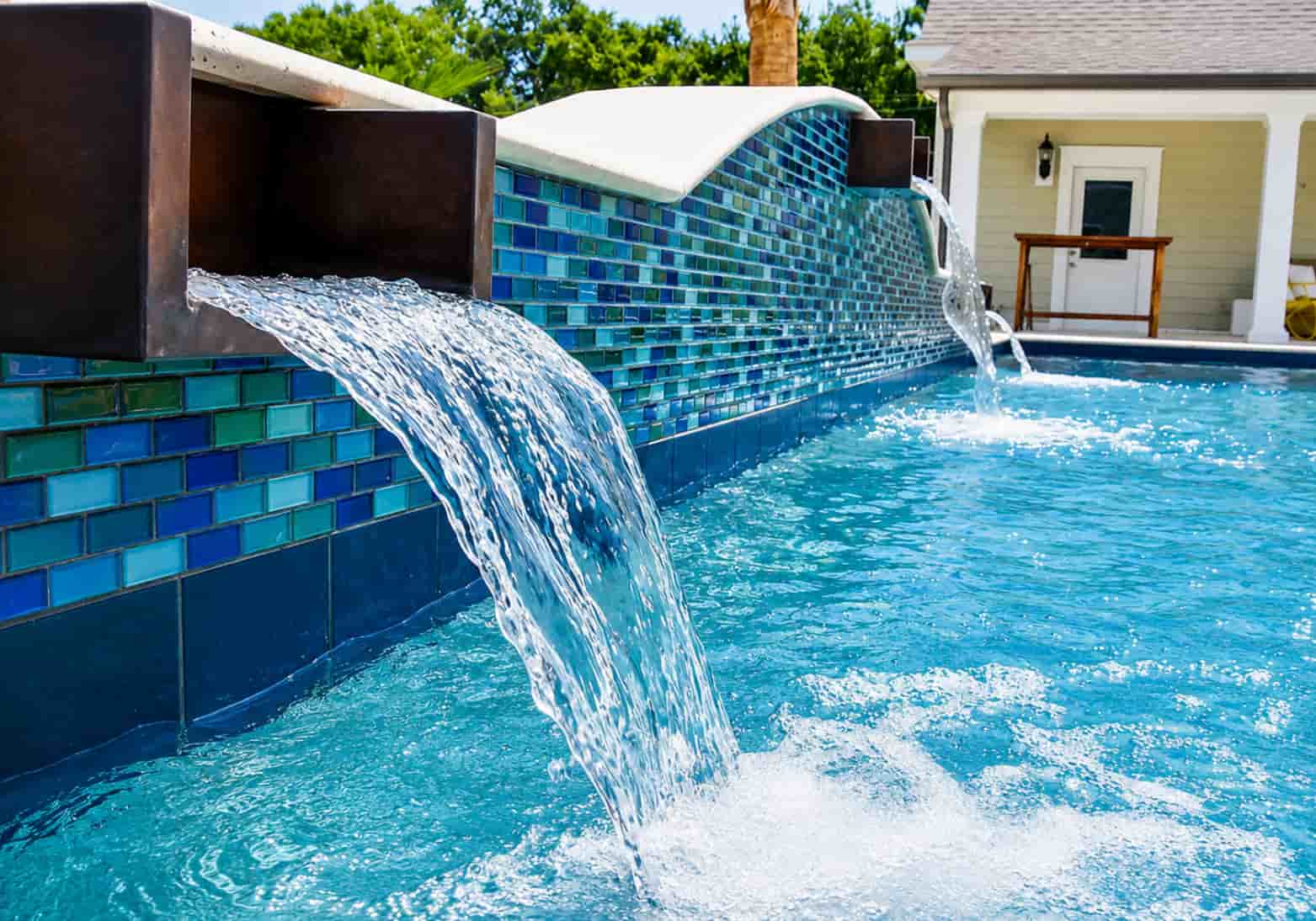 Close-up of pool scuppers pouring water over a blue and teal glass tile bond beam wall