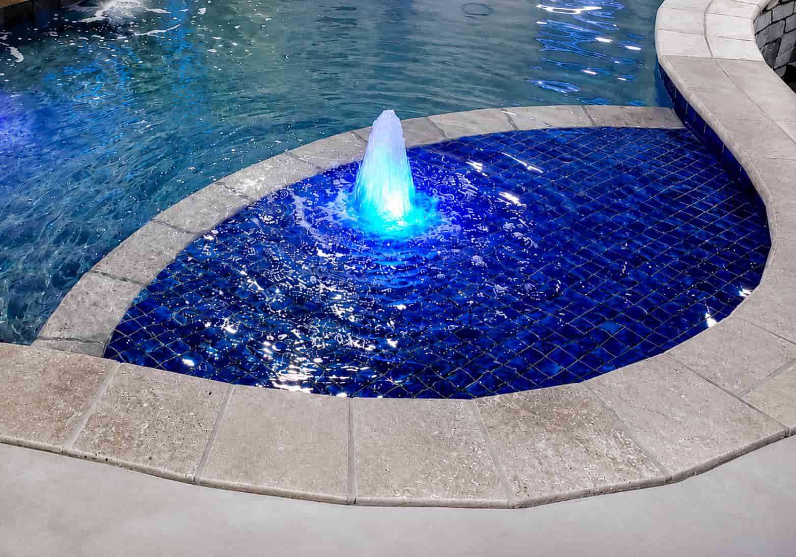 Spray fountain with blue LED lighting centered in a pool spa with cobalt blue mosaic tile