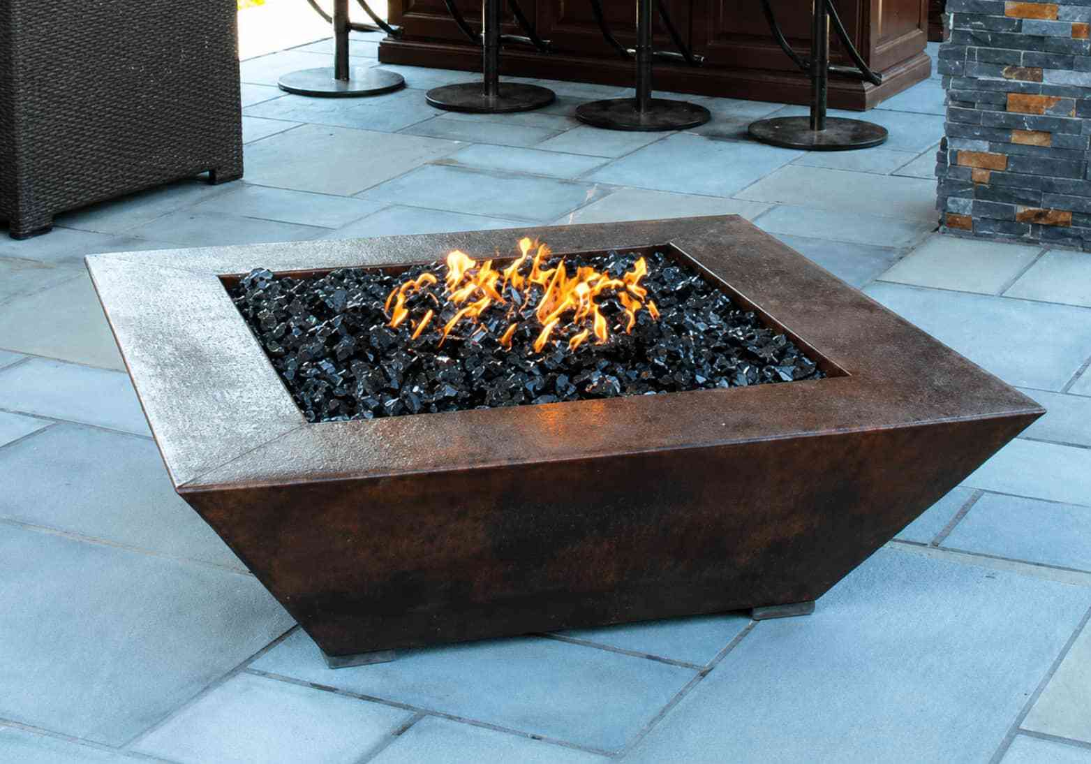 Square freestanding copper fire pit with black fire glass on bluestone patio
