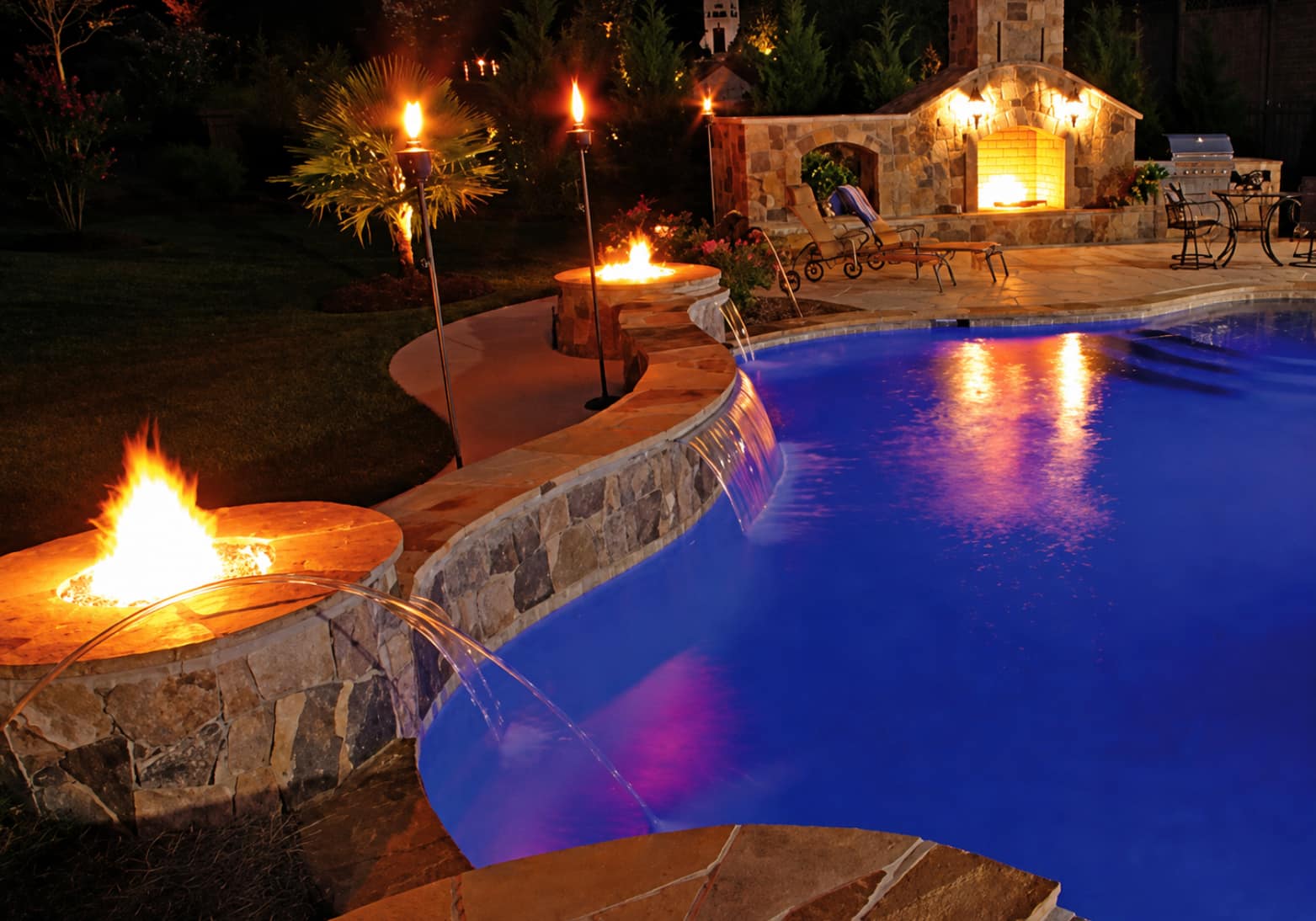 Stone fire pit integrated into curved pool perimeter wall with built-in seating at night