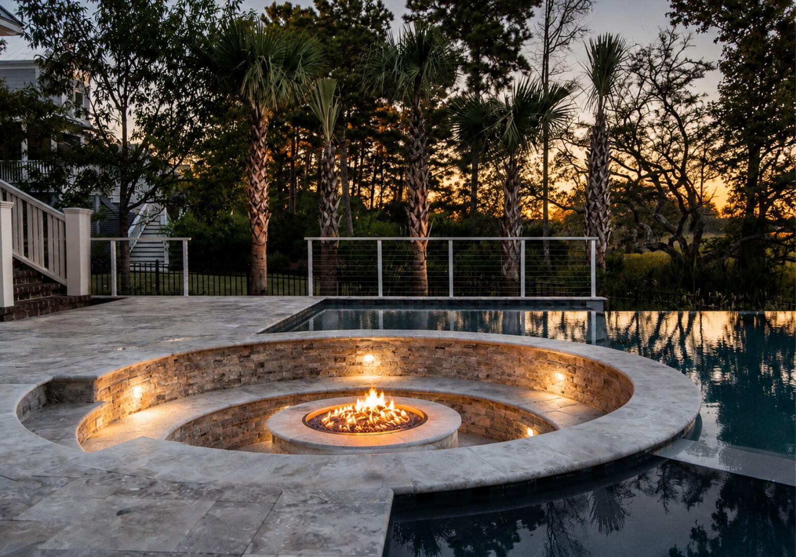 Sunken fire pit with stone seating area beside infinity pool at sunset