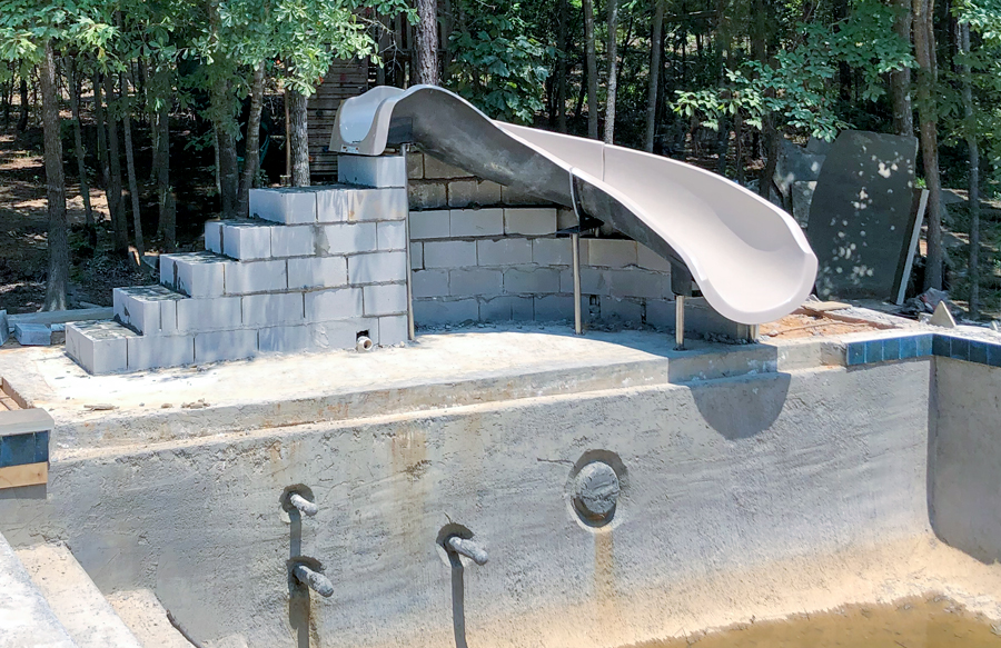 Inground pool under construction with unfinished slide structure and exposed plumbing