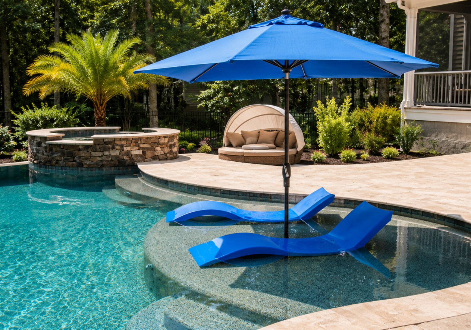 Two blue chaise lounges on a pool sun shelf with patio umbrella in a custom backyard pool