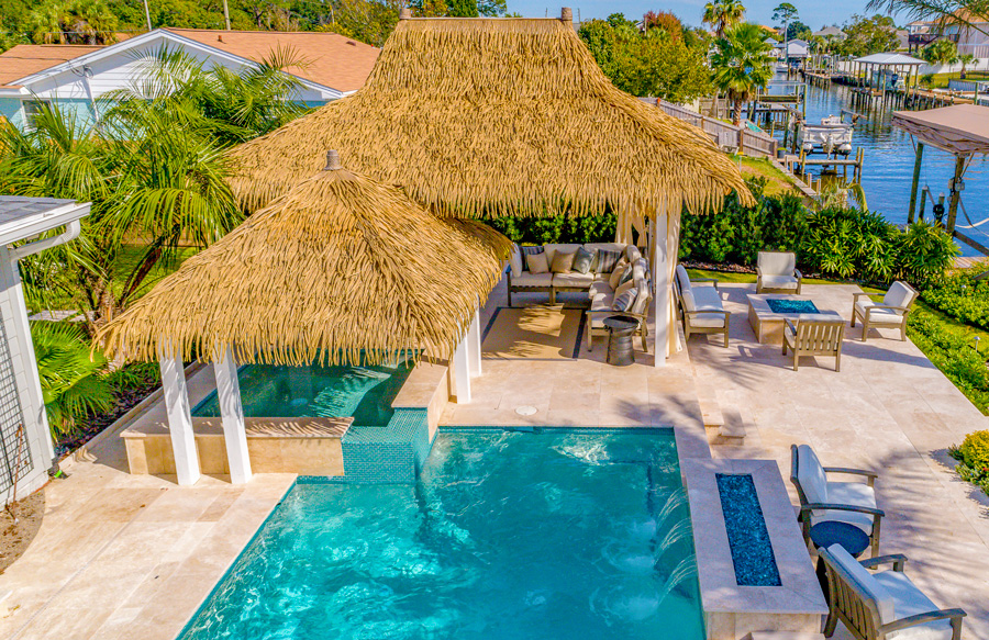 Tropical backyard pool with thatched shade structure and raised spa