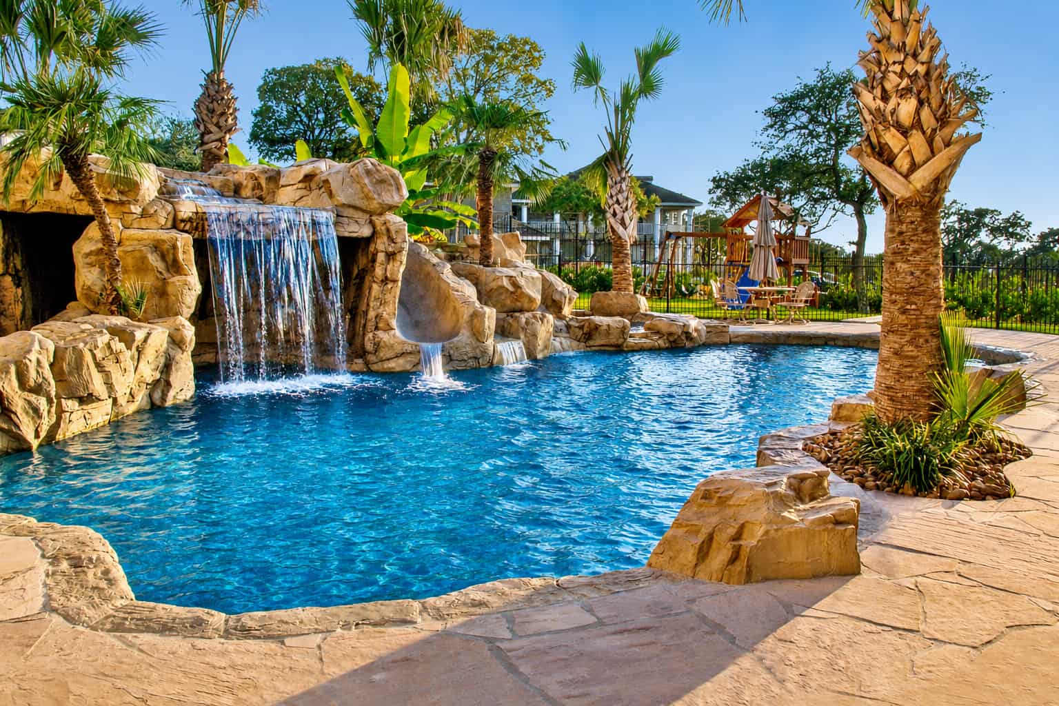 Tropical backyard pool with rock waterfall, palm trees, and patio seating area