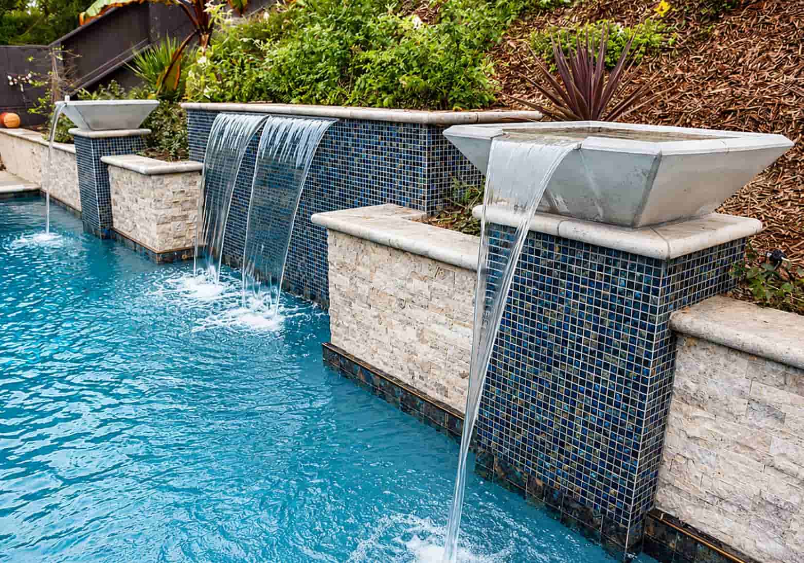 Square water bowls on stone pedestals cascading water into a pool with blue mosaic tile