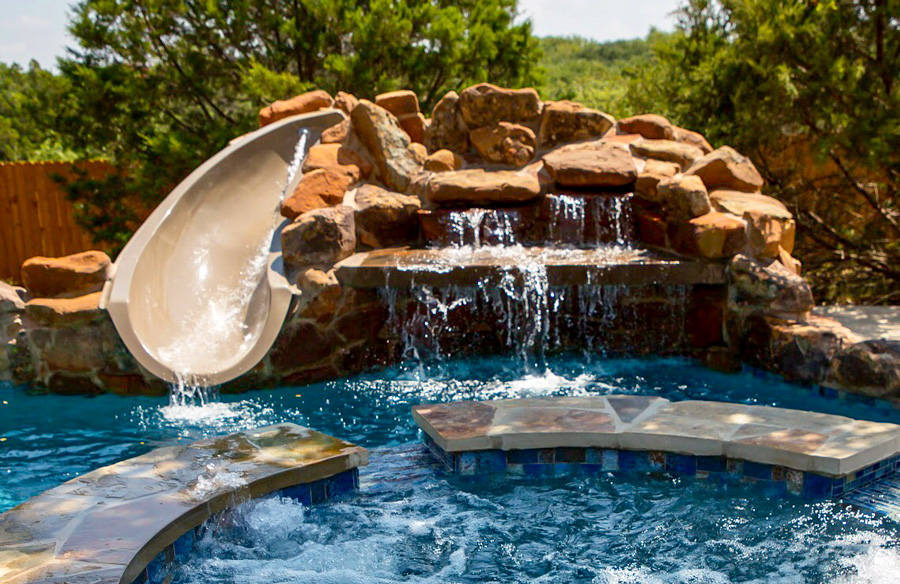 Custom pool grotto with waterfall and curved slide cascading into a spa and pool