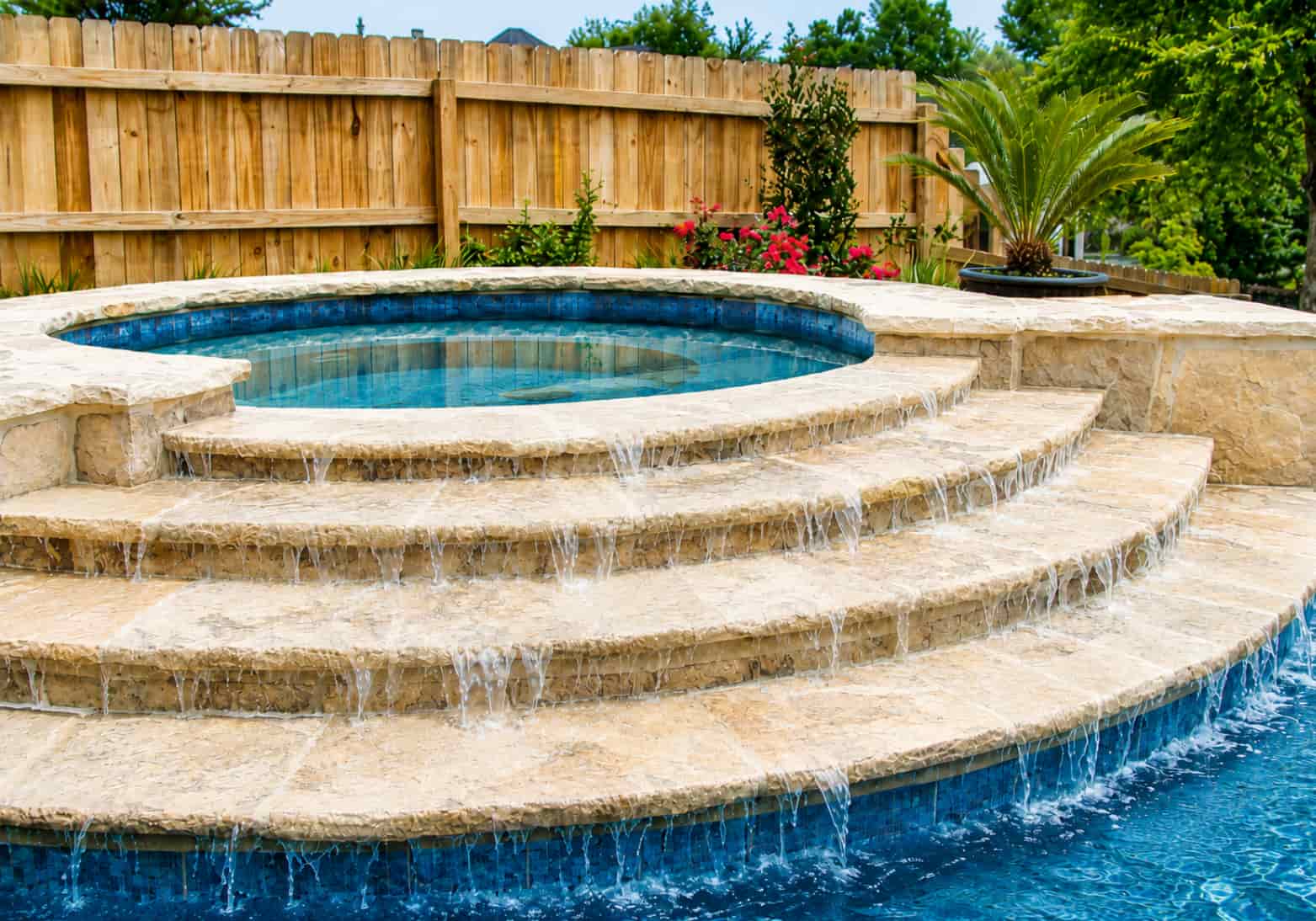 Elevated spa with a weeping spillway cascading water down stepped travertine levels into the pool